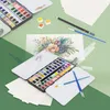 A flat lay of an art supplies set including a watercolor paint box, brushes, pencils, and paper. Podgląd zdjęcia produktu