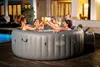 Four people are toasting drinks in a hot tub at night. Produktbild-Vorschau