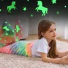 Mädchen liegt auf einem Teppich, eingewickelt in eine regenbogenfarbene Plüsch-Meerjungfrau-Schwanzdecke mit im Dunkeln leuchtenden Einhorn- und Sternmustern Produktbild-Vorschau