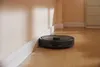 A robot vacuum cleaner is cleaning the floor next to a wall. Produktbild-Vorschau