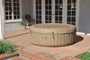An inflatable hot tub sits on a brick patio in front of a house with glass doors. Produktbild-Vorschau