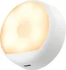A white, rounded night light with a warm yellow glow emanating from its center. Podgląd zdjęcia produktu