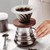 A person is making coffee using a pour-over coffee maker. There are coffee beans in a jar and a scoop nearby. Produktbild-Vorschau