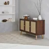 A dark wood sideboard with rattan-fronted doors is placed in a room with a light gray wall and a patterned rug. Produktbild-Vorschau