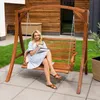 A woman is sitting on a wooden garden swing, reading a book. Náhled obrázku produktu