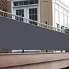 A dark gray privacy screen is attached to a balcony railing, with a wooden deck in the foreground and a building with windows and doors in the background. Produktbild-Vorschau