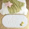 A fluffy white oval rug is placed on a wooden floor in front of a bed with a green blanket and a pink star pillow. Anteprima dell’immagine prodotto
