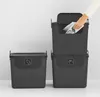 Three dark gray recycling bins are stacked and arranged in a studio setting against a light gray and white background. A hand is shown placing paper into the top bin. Produktbild-Vorschau
