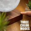 A close-up shot of a floating moon lamp on a wooden base, with a finger touching the base. There are also plants in the background. Produktbild-Vorschau