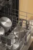 Several stainless steel pots and lids are neatly arranged in a dishwasher rack, ready for cleaning. Produktbild-Vorschau