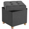 A dark gray storage ottoman with a tufted lid slightly ajar, resting on four light brown wooden legs, against a white background. Náhled obrázku produktu