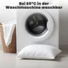 A pillow is placed in front of a washing machine, with a laundry basket to the side. Produktbild-Vorschau