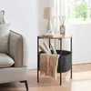 A round side table with a storage basket is placed next to a sofa, with a lamp and diffuser on top. Náhled obrázku produktu