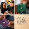 A collage of four images showing a couple interacting with advent calendars and a close-up of a calendar page, with text overlay on a wooden background. Produktbild-Vorschau