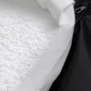 A close-up view of the interior of a product, showing white foam beads and a white fabric lining next to a black fabric exterior with a zipper. Produktbild-Vorschau