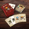 A set of One Piece themed playing cards and a tin are displayed on a wooden surface. Produktbild-Vorschau