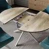 A dining table with extendable leaves, shown with teal chairs and a wooden cabinet in the background. Anteprima dell’immagine prodotto