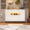 A white sideboard with LED lighting is displayed in a room with decorative items on the wall and floor. Voir les images du produit
