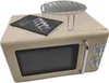 A beige retro-style microwave oven with a booklet and a wire rack on top, presented on a white background. Produktbild-Vorschau