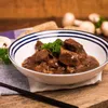 A bowl of goulash with mushrooms and bread in the background. Produktbild-Vorschau