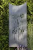 A metal garden stele with cut-out floral designs, placed outdoors in a garden setting with lush green foliage and tall grasses. Produktbild-Vorschau