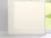 A close-up of a cream-colored sheer curtain panel, likely a sliding panel curtain, against a window with a blurred green outdoor scene. Produktbild-Vorschau