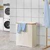 A laundry basket with a blue shirt draped over it, placed in a laundry room with washing machines and tiled walls. Produktbild-Vorschau