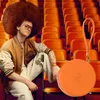 A person with an afro hairstyle sits in orange stadium seats, holding an orange round object. Voir les images du produit