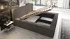 A bed with its storage compartment open, showing the slatted base and interior space. A small side table with decorative items is next to the bed. Produktbild-Vorschau