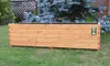 A wooden planter box sits on a grassy lawn in front of a fence and a blue spruce tree. Produktbild-Vorschau