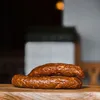 Two sausages are stacked on a wooden surface, with a blurred background. Produktbild-Vorschau