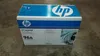 A cardboard box for an HP LaserJet toner cartridge sits on a concrete floor. Náhled obrázku produktu