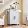 A white kitchen cart with a wooden top is shown in a room with a chair and curtains. Produktbild-Vorschau