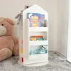 A white rotating bookshelf for children's toys and books, placed on a gray carpet next to a large teddy bear. Podgląd zdjęcia produktu