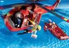 A red rescue helicopter is hovering over blue water, with a rescue boat nearby. A figure is being lowered from the helicopter to the boat. Náhľad obrázku produktu