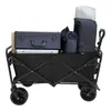 A black folding wagon filled with various items, including a dark blue suitcase, a silver laptop or case, and several dark blue bags, with a white cylindrical item on top. Náhled obrázku produktu