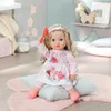 A doll sitting on a pillow on a rug, holding a brush. Produktbild-Vorschau