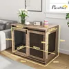 A dog crate furniture piece is shown in a living room setting next to a sofa, with decorative items on top. Produktbild-Vorschau