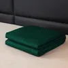 A folded green blanket is placed on a light-colored surface in front of a black headboard. Podgląd zdjęcia produktu