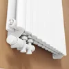 A close-up, low-angle view of the bottom section of a white radiator, showing its valve and connection pipes against a brown wall. Podgląd zdjęcia produktu
