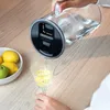 A person is pouring water from a filter jug into a glass. There are lemons and a pear in a bowl nearby. Podgląd zdjęcia produktu
