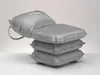 A gray inflatable bathing cushion is stacked on top of three other cushions, with a light gray background. Produktbild-Vorschau