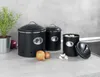 Three black storage containers with silver accents are arranged on a countertop, with onions and garlic nearby. Produktbild-Vorschau