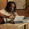 A man is using an iPad with a keyboard case on a wooden desk. Voir les images du produit