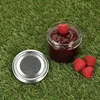 A jar of raspberry jam with a lid and raspberries on grass. Anteprima dell’immagine prodotto