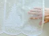 A hand is holding up a white lace curtain with a Christmas tree and gift pattern. Produktbild-Vorschau
