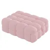 A light pink, plush ottoman with a tufted, segmented design, shown from a three-quarter side view. Podgląd zdjęcia produktu