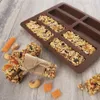 A silicone mold for making granola bars, with several finished granola bars and some loose ingredients on a wooden surface. Anteprima dell’immagine prodotto