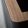 A close-up shot of the corner of a modern trash can, showing the texture of the wood lid and the matte black body. Produktbild-Vorschau