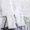 A close-up view of white sheer curtains with text printed on them, layered over a magazine or book with images of greenery. Produktbild-Vorschau